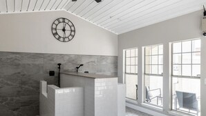 Ein Badezimmer mit einem weißen Waschbecken, einer großen Uhr und einem Fenster mit Blick ins Freie.
