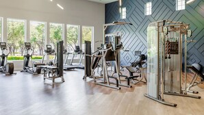 Ein modernes Fitnessstudio mit verschiedenen Trainingsgeräten, großen Fenstern und einem geometrischen Wanddesign.
