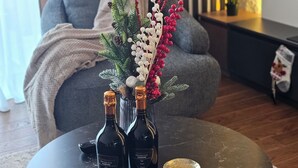 A modern living room with a grey sofa, a decorative plant arrangement, and three bottles of Prosecco on a round table.