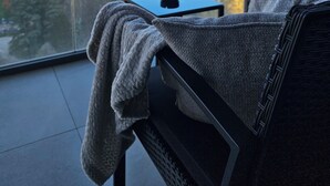 A balcony with a view of a cityscape, a table with a cup, and a chair with a blanket.