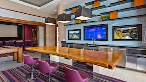 A modern kitchen with a wooden bar, purple bar stools, and a large flat-screen TV mounted above the counter. - Landing | Beautiful 2BD, Gym, Clubhouse (Cedar Park)