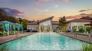 A rectangular swimming pool with a tiled edge, surrounded by a brick walkway. There are lounge chairs and a covered area with blue curtains. - Landing | Beautiful 2BD, Gym, Clubhouse (Cedar Park)