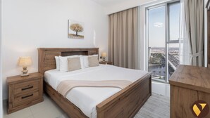 Een moderne hotelkamer met een houten bed, nachtkastje, lamp, schilderij en een groot raam met gordijnen.