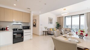 Een moderne keuken met een magnetron, fornuis en oven, een eethoek met een tafel gedekt voor twee personen, en een woonkamer met een bank en een groot raam.