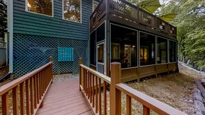 Une terrasse en bois qui mène à un espace extérieur abrité, d’où l’on peut admirer une maison et des arbres.