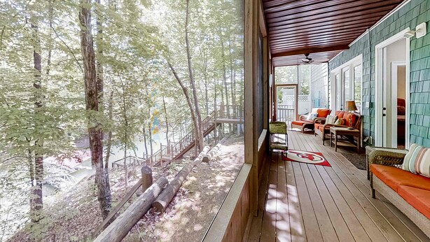 Une véranda couverte avec un plancher en bois, un coin salon avec des coussins orange et une vue sur une zone boisée.