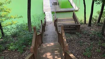 Un escalier en bois mène à une jetée surmontée d’un toit rouge, le tout étant entouré d’arbres et bordé par une étendue d’eau verdoyante.