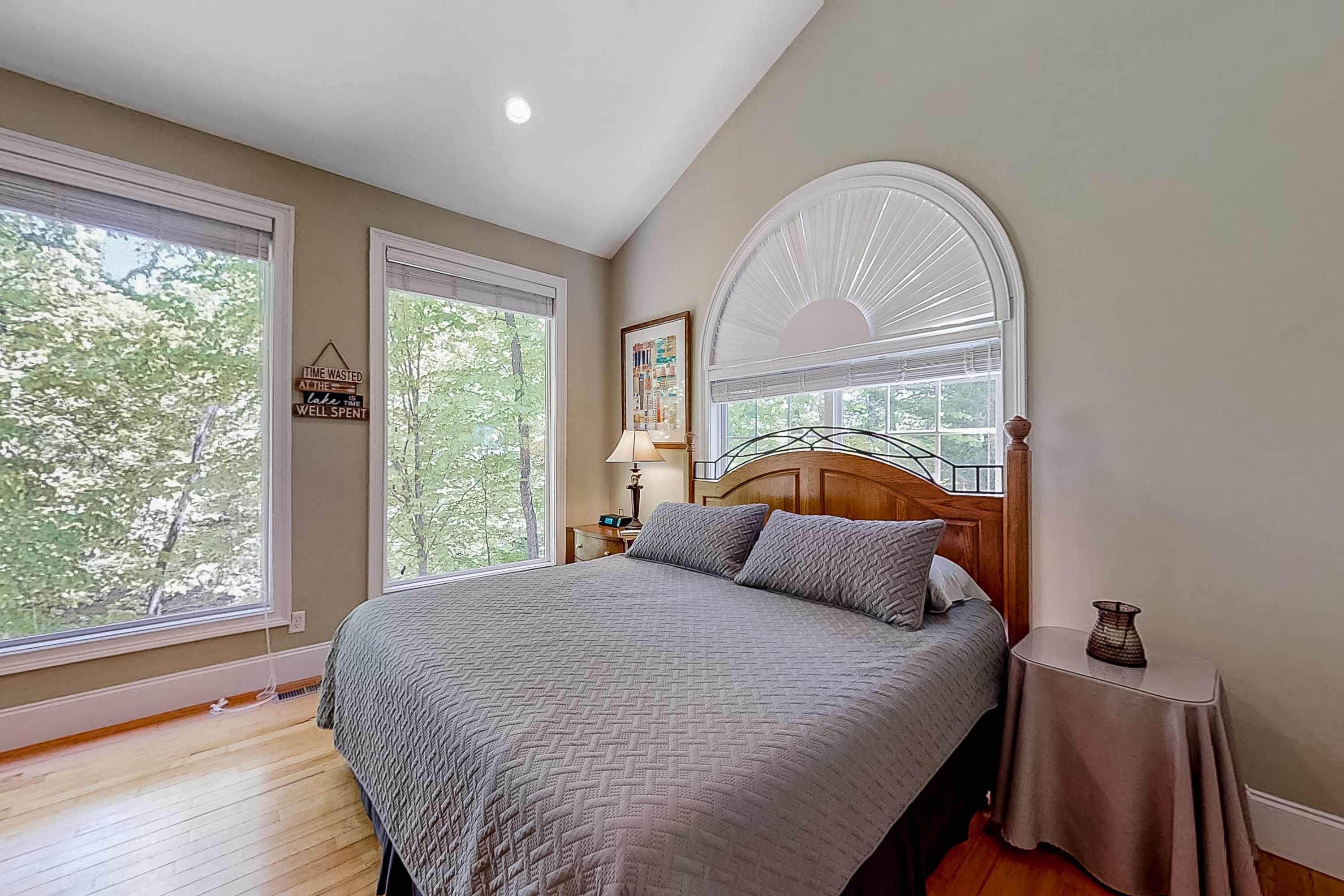Quarto com uma cama grande, duas janelas, uma mesa de cabeceira e um abajur.