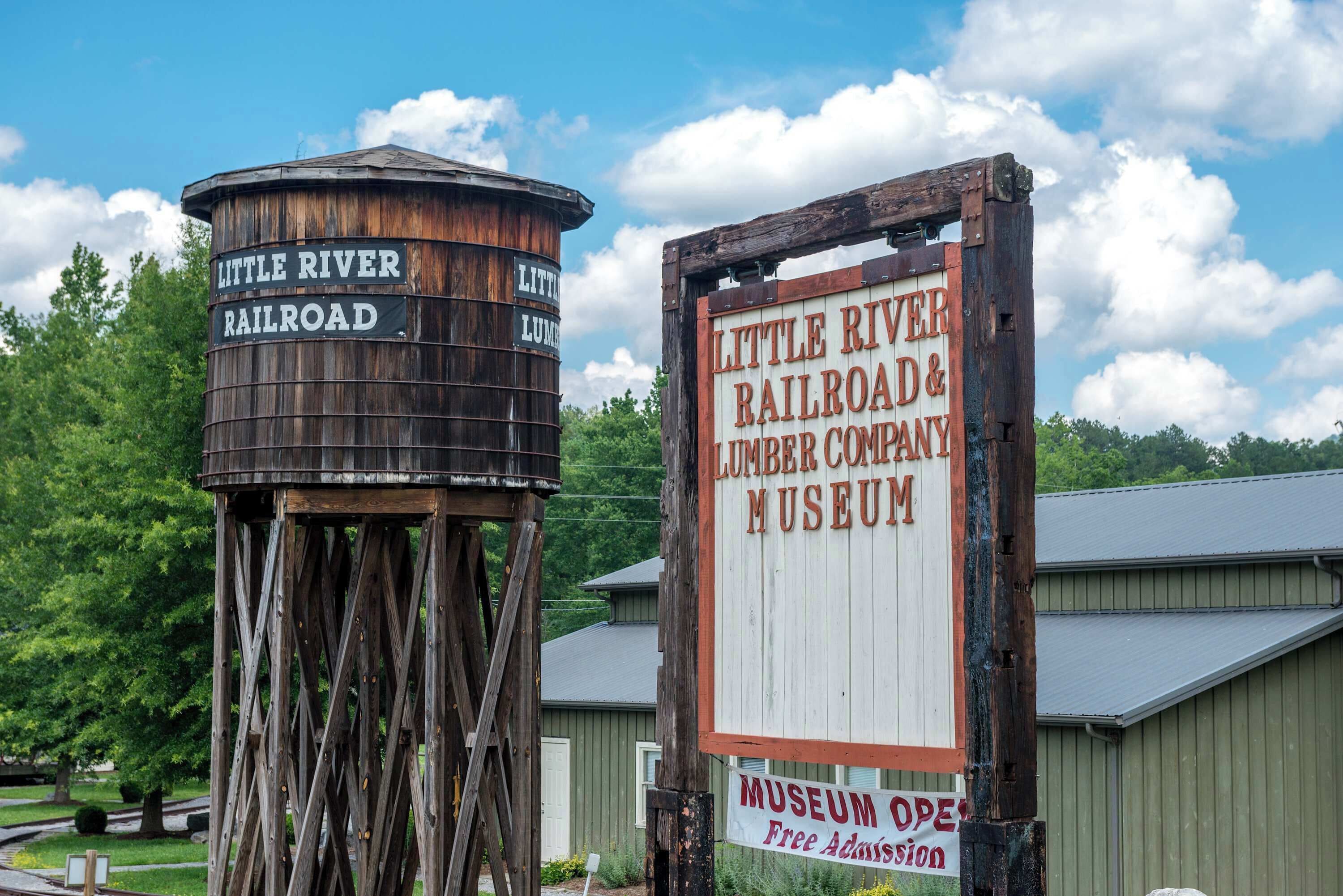 A rustic water tower and a wooden sign for the Little River Railroad & Lumber Company Museum with a free admission notice.