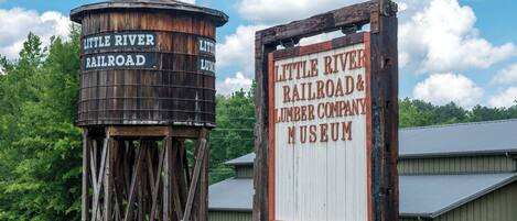 A rustic water tower and a wooden sign for the Little River Railroad & Lumber Company Museum with a free admission notice.