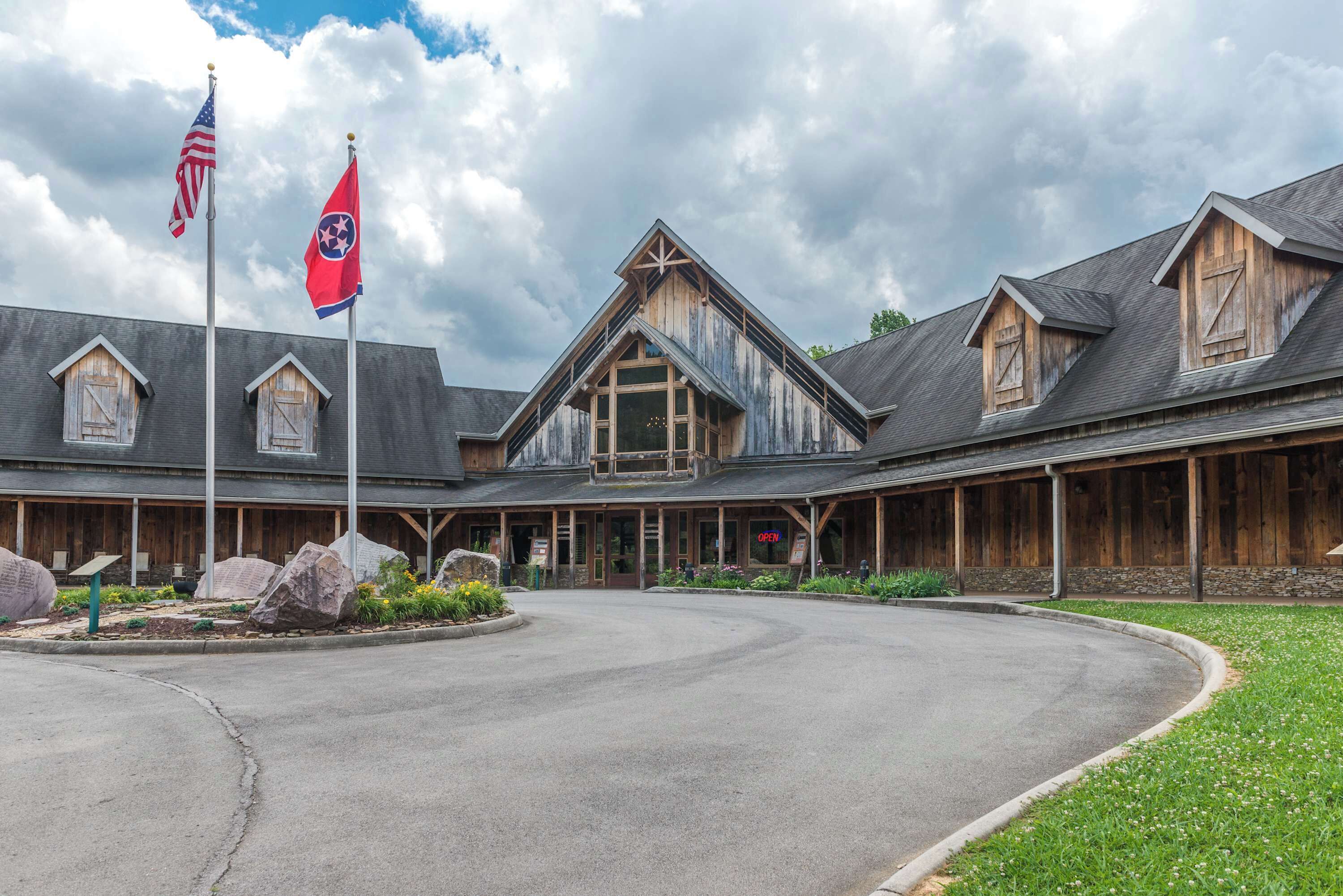 A rustic lodge with a large central building, a covered outdoor seating area, and a paved driveway.
