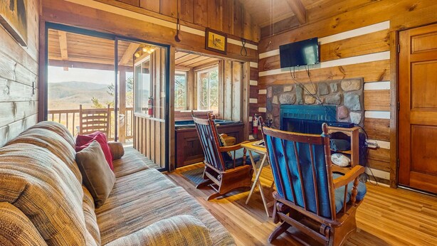 A cozy cabin interior with a wooden interior, a sofa, rocking chairs, a stone fireplace, and a television mounted on the wall. - 1 mile from Historic Townsend・Hot Tub・Fireplace (Townsend)