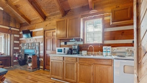 A wooden cabin kitchen with a stone fireplace, wooden cabinets, a microwave, coffee maker, and a stove. - 1 mile from Historic Townsend・Hot Tub・Fireplace (Townsend)