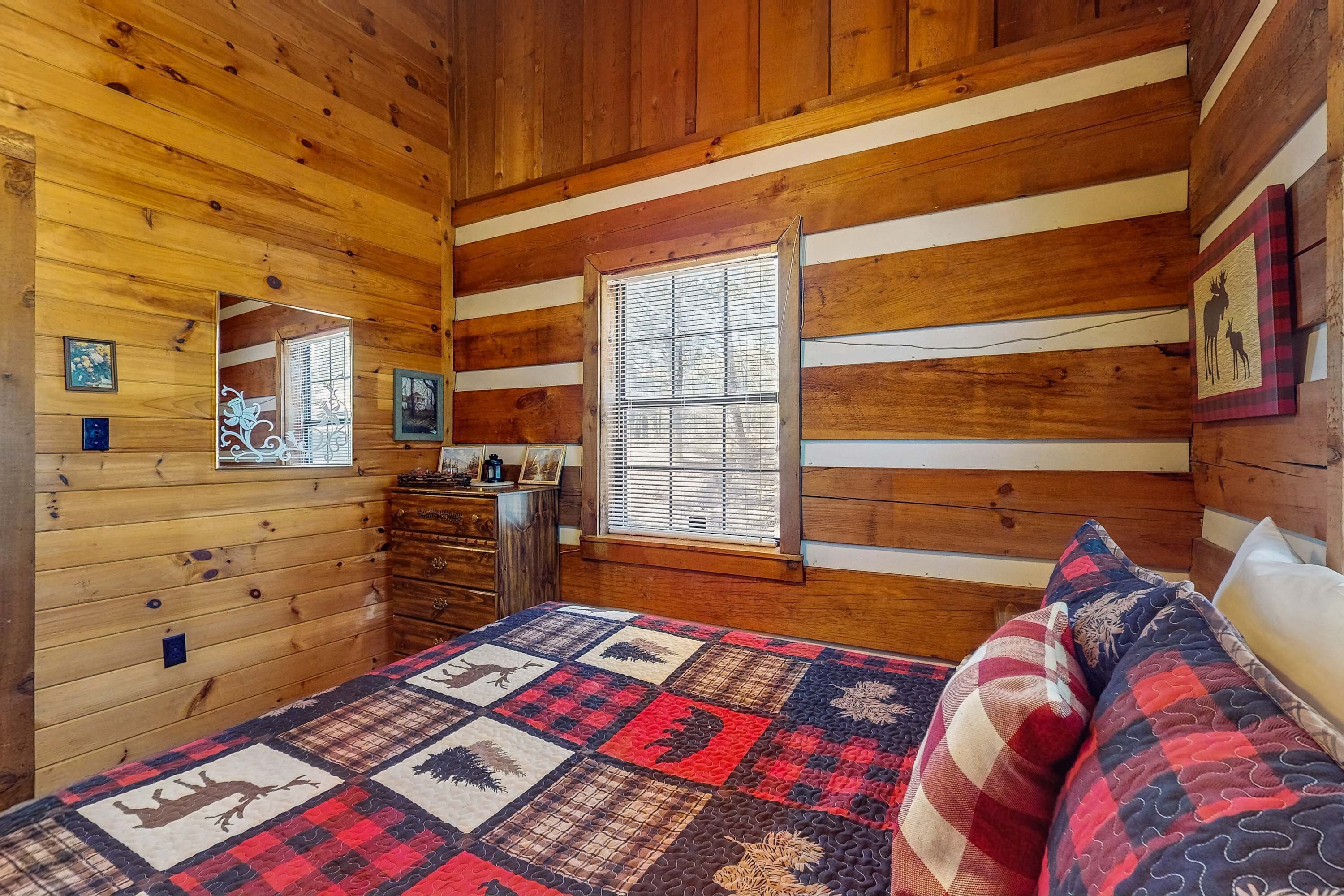 A wooden cabin bedroom with a bed, dresser, and window.