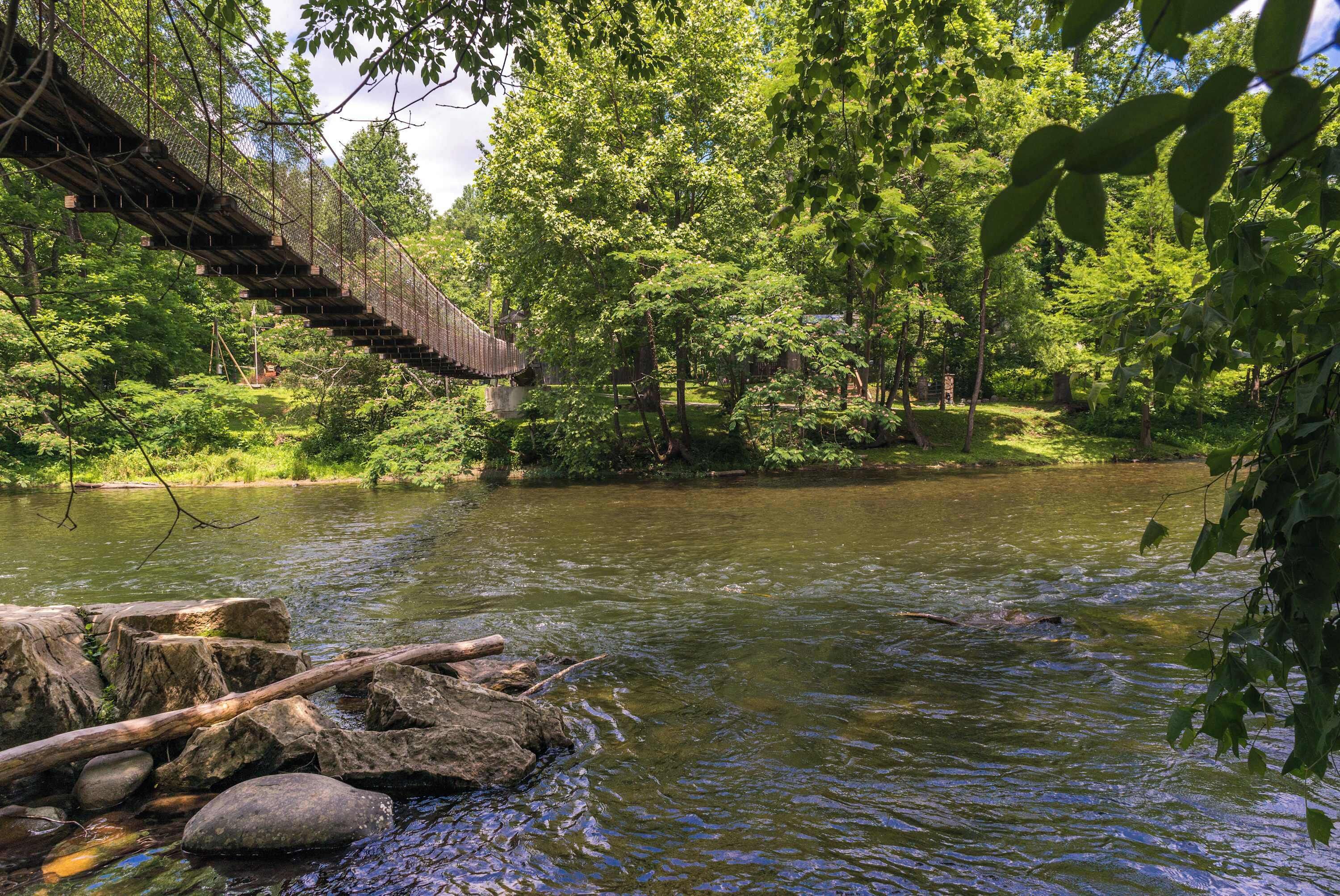 A wooden suspension bridge over a river surrounded by dense greenery.