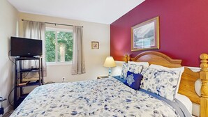 Una camera da letto con un letto, una televisione su un mobile, una finestra con tende e un quadro appeso al muro.