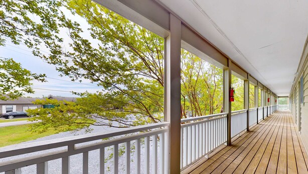 A covered wooden deck with white railings, overlooking a grassy area with trees and a building in the background. - Studio W Quiet View, Patio, Gym, Games, Dog Friendly (Baneberry)