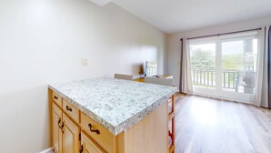 A kitchen with a granite countertop, wooden cabinets, and a large sliding glass door leading to a balcony. - Studio W Quiet View, Patio, Gym, Games, Dog Friendly (Baneberry)