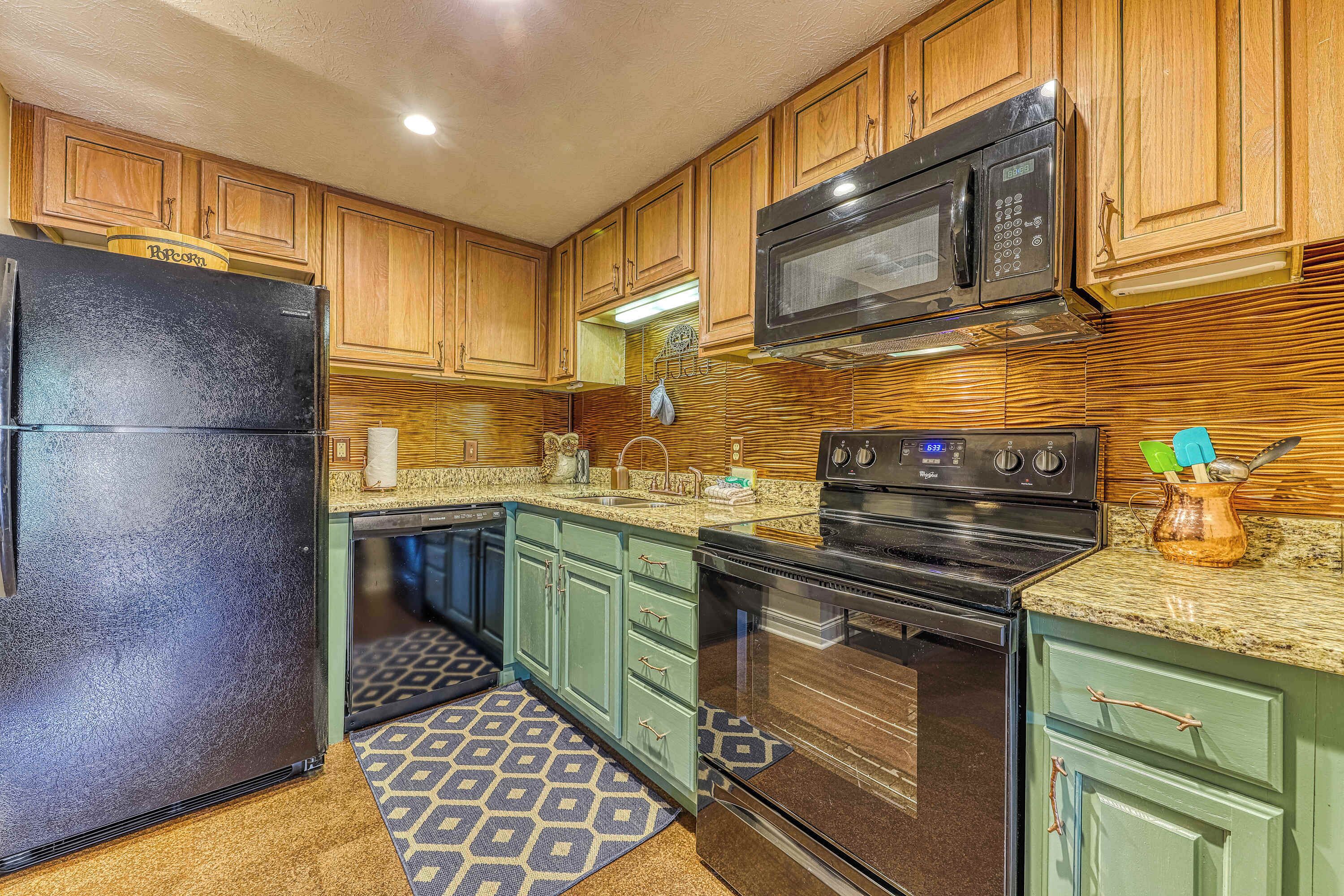 A kitchen with wooden cabinets, a black refrigerator, a microwave, a stove, and a patterned rug.