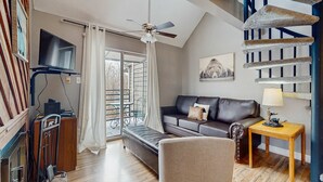 Un salon moderne avec un canapé, une table en bois, un ventilateur de plafond et un téléviseur fixé au mur.