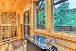 Un intérieur en bois avec une table de billard dont le plateau est en verre, de grandes fenêtres et un mur en pierre.