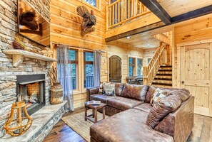 Un intérieur de chalet chaleureux avec une cheminée en pierre, un canapé en cuir, des murs en bois et un escalier.