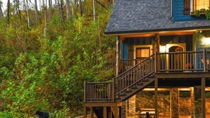 A cabin with a stone foundation, wooden deck, and a staircase leading to a balcony. - Creekside Luxury Cabin, Hot Tub, Near Downtown (Gatlinburg)