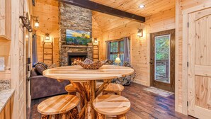 A wooden interior with a stone fireplace, round wooden table with stools, and a stone wall. - Creekside Luxury Cabin, Hot Tub, Near Downtown (Gatlinburg)