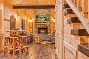 Ein Blockhaus-Interieur mit Kamin aus Stein, Holzmöbeln und einer Wendeltreppe.