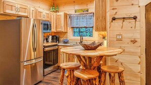 A wooden cabin kitchen with a stainless steel refrigerator, a microwave, a sink, and a wooden dining table with stools. - Creekside Luxury Cabin, Hot Tub, Near Downtown (Gatlinburg)