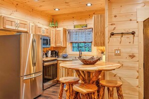 Ein Holzblockhaus-Innenraum mit einem Edelstahlkühlschrank, einer Mikrowelle, einem Holztisch mit Hockern und einem Schild mit der Aufschrift 'Tuckaleecce CAVERN'