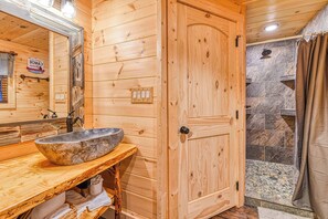 Une salle de bain en bois avec un lavabo en pierre, un miroir, une douche avec un mur en pierre et une porte en bois.