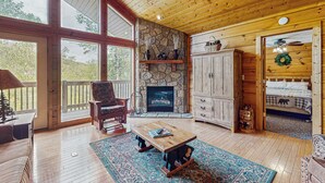 Ein gemütliches Blockhaus-Interieur mit Kamin aus Stein, Holzmöbeln und großen Fenstern mit Blick ins Freie.