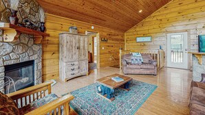 Ein gemütliches Blockhaus-Interieur mit Kamin aus Stein, Holzwänden und -decke sowie einem großen Fenster.