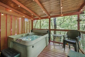 A hot tub on a wooden deck with a table and chair, surrounded by trees. - 3 Bears Cabin, Sleeps 6, Dog Welcome, Hot Tub (Sevierville)