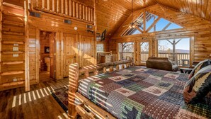 A log cabin interior with a large bed, a balcony, and a loft area. - Mtn Retreat, for 12・Hot Tub・Games・Deck・Shared Pool (Sevierville)