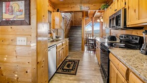 A wooden cabin interior with a kitchen, dining area, and a staircase leading to a loft bedroom. - Mtn Retreat, for 12・Hot Tub・Games・Deck・Shared Pool (Sevierville)