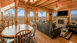 A wooden cabin interior with a dining table, chairs, a sofa, and a fireplace. - Mtn Retreat, for 12・Hot Tub・Games・Deck・Shared Pool (Sevierville)
