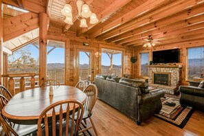 A wooden cabin interior with a dining table, chairs, a sofa, and a fireplace. - Mtn Retreat, for 12・Hot Tub・Games・Deck・Shared Pool (Sevierville)