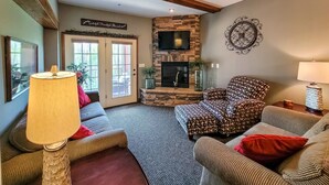 A living room with a stone fireplace, a television mounted above it, and a patterned armchair. - Charming Dollywood Retreat・Hot Tub & Pool Access (Sevierville)