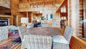 Ein großzügiges Blockhaus-Interieur mit einer zentralen Sitzecke, einem Kamin und einem Balkon.