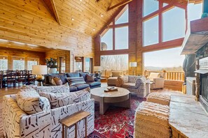 A spacious living room with a high ceiling, large windows, and a fireplace. - Luxe Gatlinburg Cabin・Hot Tub・Foosball・Pool table (Gatlinburg)