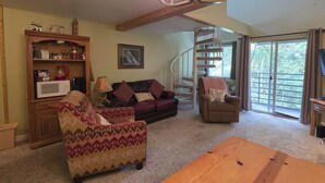 A spacious living room with a wooden ceiling, a spiral staircase, and a large window offering a view of greenery. - Gatlinburg Condo, for 6・Pools・Hot Tub・Lovely Views (Gatlinburg)