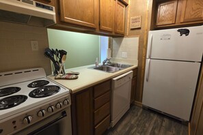 A kitchen with wooden cabinets, a white stove, a dishwasher, and a refrigerator. - Ski Mountain Condo | Stunning Views & Balcony (Gatlinburg)