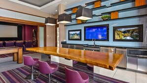Una cocina moderna con una barra de madera, taburetes de barra morados y un televisor de pantalla plana grande montado sobre la encimera.