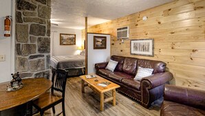 Una habitación acogedora con pared de piedra, paneles de madera, un sofá de cuero, una mesa de madera y una cama con cabecera de madera.