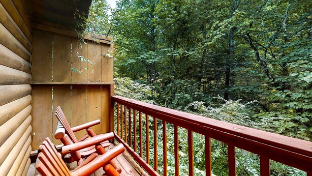 Una cabaña de madera con barandilla roja que da a un bosque denso.