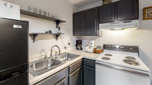 Cocina compacta con refrigerador, pileta doble, estufa y alacenas oscuras.