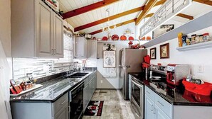 Una cocina con armarios blancos, encimera negra y electrodoméstico rojo.