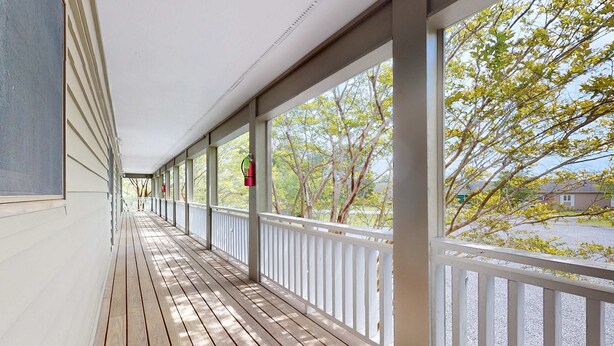 A covered porch with a wooden floor and white railings, overlooking a street with trees and a building in the background. - Relaxing Studio, Sleeps 2, Near Golf & Douglas Lake (Baneberry)